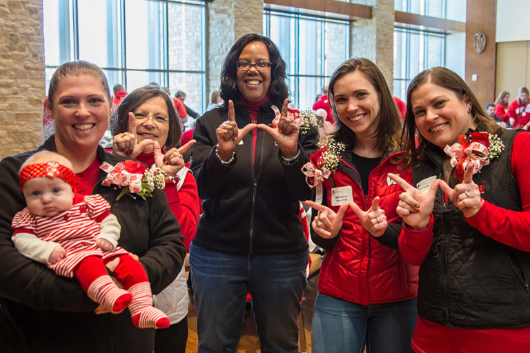 photo of School of Nursing Dean Linda Scott with School of Nursing alumni dressed in Badger red, making the Wisconsin "W" symbol with their hands
