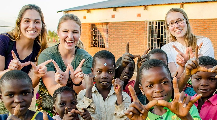 Student Nurses in Malawi, posing with Malawi children making the "W" symbol with their hands