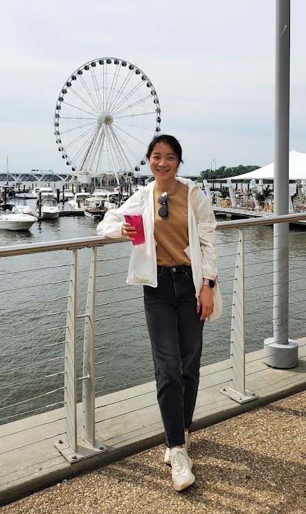 Effy Yu stands next to railing with water and ferris wheel in background
